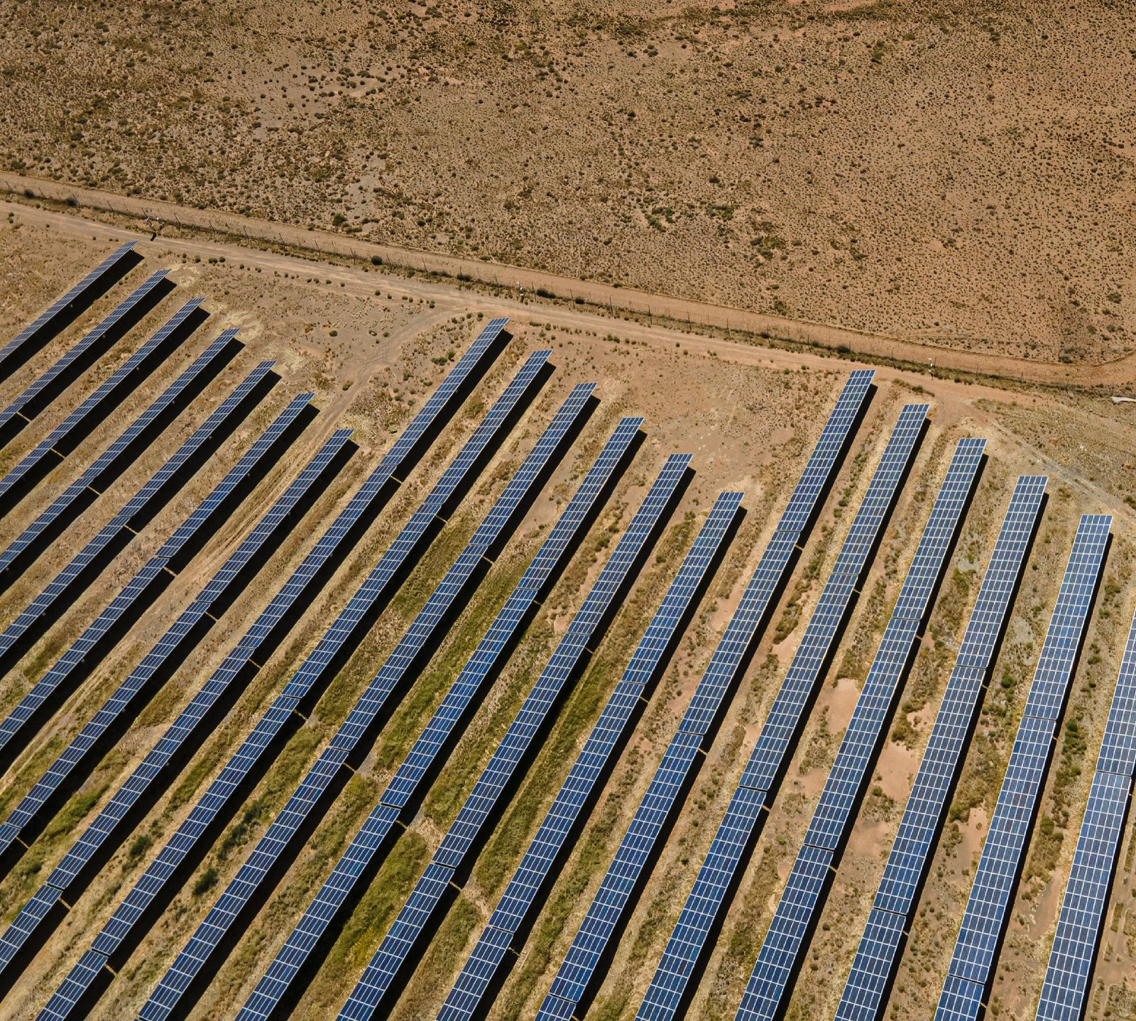 Vue aérienne d'une centrale solaire, rangées de panneaux alignées sur un sol aride.